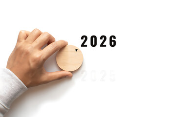 A hand selects a wooden disc with "2026" on it, signifying a choice and a plan for the new year.