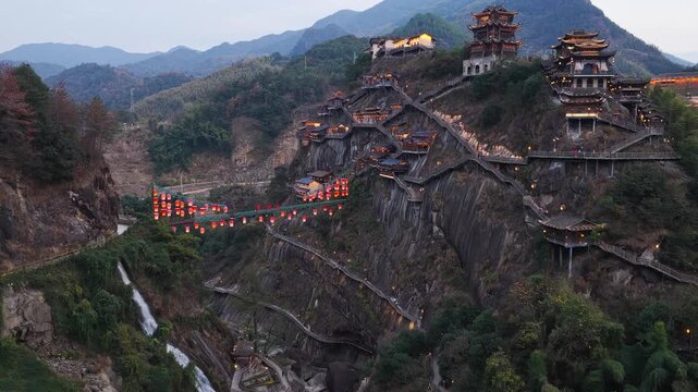 Aerial view of illuminated buildings and walkways clinging to steep cliffs in Wangxian Valley, with mountains in the background, Wangxian Valley, China.