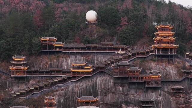 Aerial view of Wangxian Valley's traditional buildings cascading down the cliffside, with a striking white sphere atop the hill, Wangxian, China.