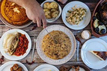 Person slicing spanish tortilla de patatas with various tapas dishes