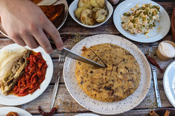 Hand cutting traditional spanish tortilla with various tapas