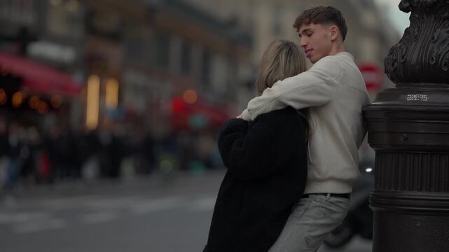 A young couple embraces on a street corner in Paris France The lovers are hugging near a vintage lamp post sharing a romantic moment in the city of lovers.