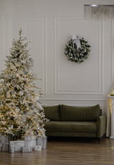 A bright room with a green sofa and a decorated white Christmas tree with yellow lights