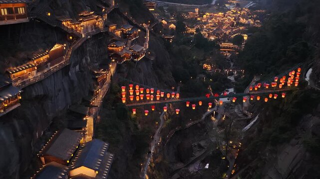 Aerial view of Wangxian Valley's illuminated buildings and red lanterns contrasting with the dark cliffs at night, Wangxian Valley, China.