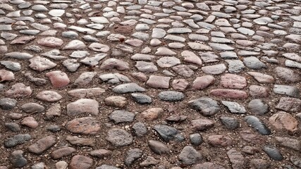 Traditional cobblestone pavement texture with rounded stones in gray and pink tones, wet historic street surface after rain, european old town road background for urban design.
