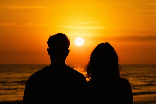 Romantic couple silhouette watching vibrant sunset over ocean waves