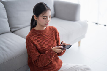 Asian Woman controlling smart home. mobile phone with smart home app in living room. touch screen ai technology. Remote home control system