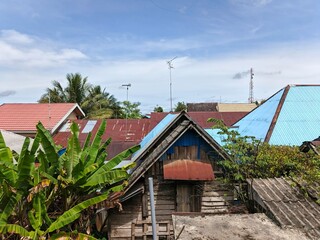 Residential houses and protected green trees against a backdrop of a bright, slightly cloudy sky.