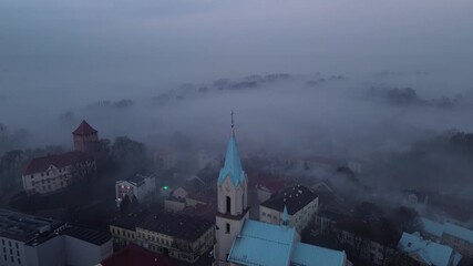 Drone ascending above fog revealing church cross in Oswiecim, Poland