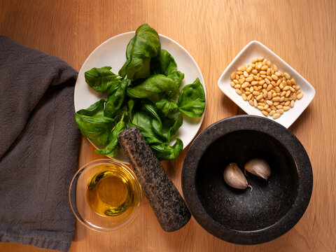 Flatlay with ingredients and kitchen tool to make pesto, such as basil, garlic, olive oil and pine nuts. Black mortar as tool to grind the ingredients.