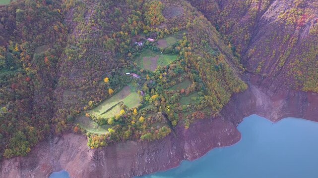Aerial video of hillside farms and autumn forest above the turquoise waters of Lake Fierza in northern Albania.