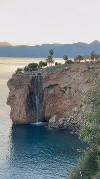 Small waterfall in Falez Park, Muratpasa, Antalya. Sunset light behind distant mountains, Mediterranean Sea in the background, urban nature, and coastal landscape