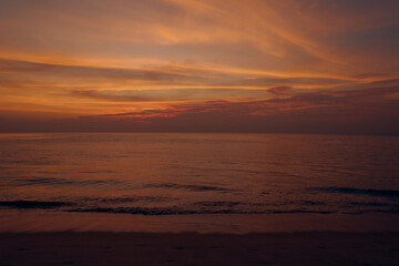 Gentle waves meet the smooth shoreline under a glowing, cloud-filled sky, creating a calming scene of beauty, peace, and the end of a summer day. Natai Beach, Phang Nga, Thailand