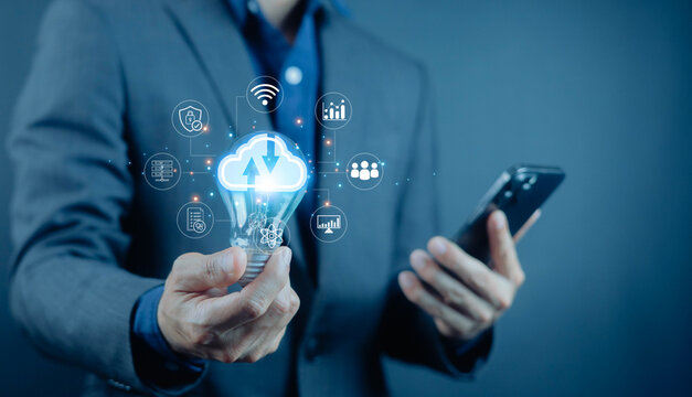 Businessman holding smartphone and light bulb with cloud computing icons, representing smart technology, digital innovation, cloud network, data security, mobile solutions. - Powered by Adobe