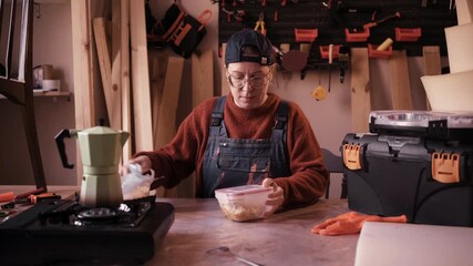 Female carpenter sitting at wooden workbench having lunch break in workshop - Powered by Adobe