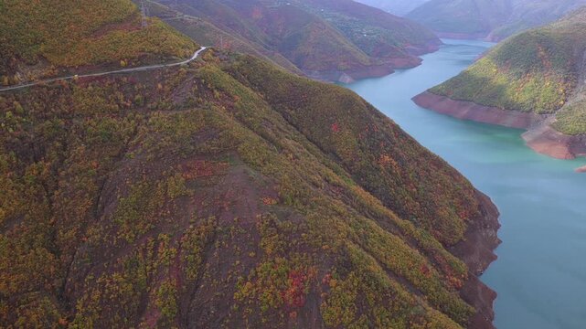Aerial video of the autumn-covered mountains and winding road above Lake Fierza in northern Albania.