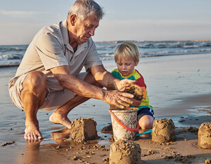 Dziadek uczący wnuka stawiać babki z piasku na plaży