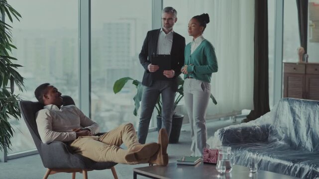 White agent reviews closing details while relaxed buyer observes cityscape during contract signing process