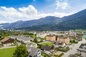 Aerial view of houses and buildings nestled in a valley beneath towering mountains, a vibrant contrast of urban and natural landscapes, Treptower Park, Berlin, Germany.