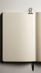 An open blank notebook with a binder clip and bookmark ribbon on a light surface.