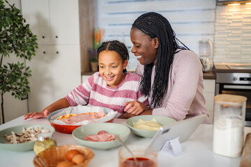Mother and daughter making pizza using digital tablet in kitchen