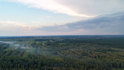 Aerial view of lush green fields and forests under a cloudy sky at sunset, depicting natural beauty and tranquility in rural landscape settings.