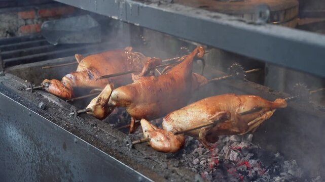 Whole ducks roasting on rotating spits over charcoal grill at street food stall