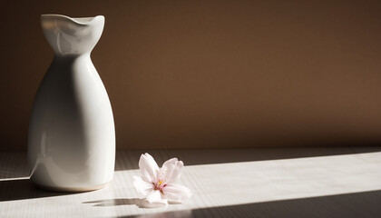 日差しが差し込む木目テーブルの白い徳利と桜一輪