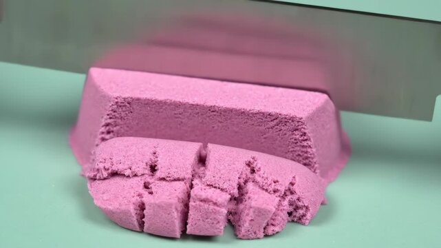 A knife cutting and slicing pink kinetic sand in a close-up shot. Oddly satisfying ASMR video for relaxation and stress relief.