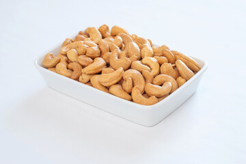 Premium grade, whole roasted cashew nuts in a white ceramic bowl on a white table.