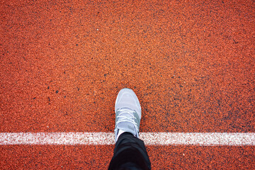 Lone sports person positions on bright red track surface emphasizing commitment and concentration