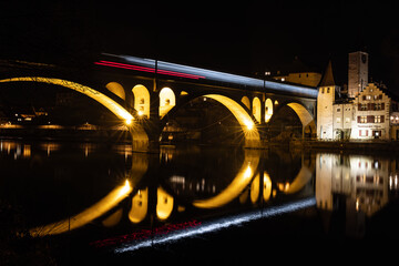 long exposure of a train passing the illuminated railroad bridge of Bremgarten, which is reflecting in the Reuss river