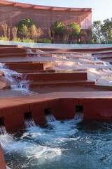 Water amphitheater or canyon in Krasnodar's city park or Galitsky Park. Architectural landscape with cascading red terraces over which water flows. Plants grow along curved red wall. Fall 2025..
