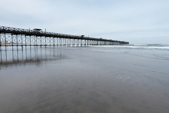 Long pimentel fishing pier extending into the pacific ocean from a reflective sandy beach on an overcast day