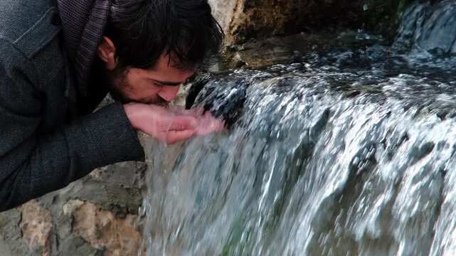 Man scooping fresh spring water from a small waterfall with cupped hands, quenching thirst in nature &mdash; pure, hydrating, refreshing moment highlighting wellness and conservation