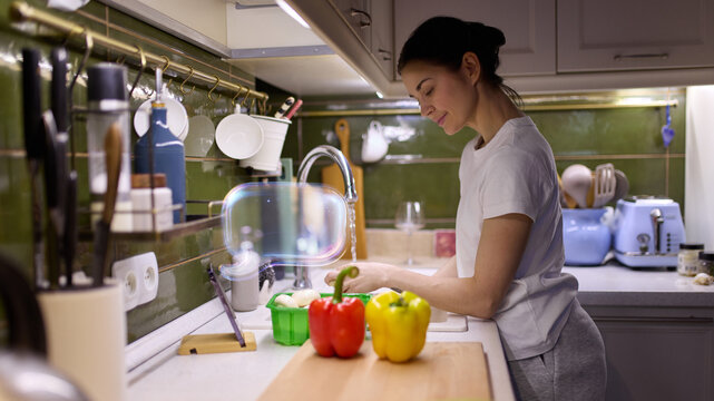 Woman interacting with AI kitchen assistant while cooking vegetables in modern interior. Concept of AI collaboration, smart home assistance, intuitive cooking experience, digital lifestyle comfort.