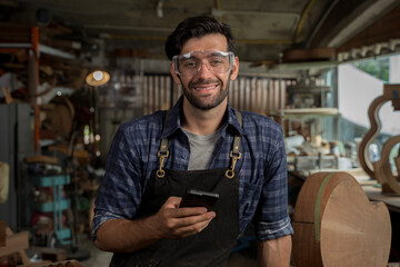 Smiling Carpenter in Workshop Using Smartphone, Craftsman Wearing Safety Goggles and Apron