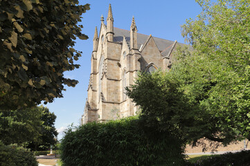 The Gothic &Eacute;glise Saint-L&eacute;onard in Foug&egrave;res, France, showcasing its impressive stone facade and decorative spires, beautifully framed by the lush greenery of the town public gardens