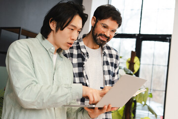 Two multinational men collaborating, studying, taking notes using laptop, working in modern office