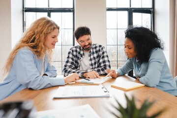 Diverse group of smiling multinational team collaborating on paperwork in modern office