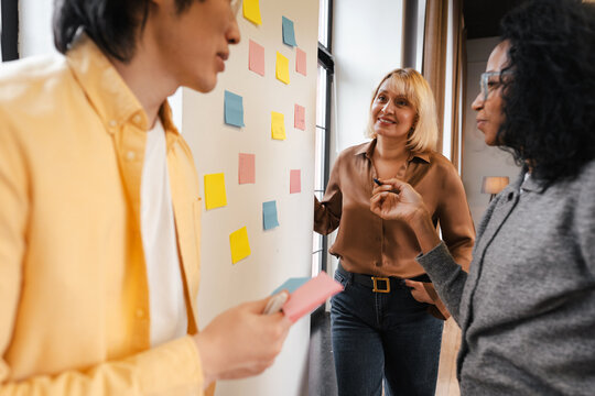 Diverse business team collaborating with sticky notes on wall in modern office