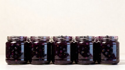 Row of glass jars with preserved mood representing homemade berry storage against neutral background with copy space