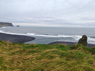 Dramatic black sand beach in Iceland with basalt cliffs and sea stacks. Stunning volcanic landscape of Reynisfjara coast under a moody sky. Scenic Nordic nature.