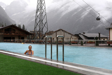 Woman relaxing in outdoor swimming pool with scenic mountain and village view
