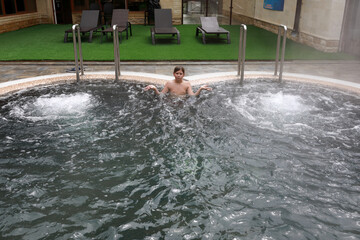 Young boy relaxing in bubbling outdoor hot tub with confused expression