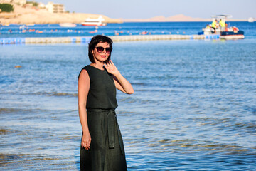 A grown woman casual clothes stands knee-deep in ocean water.