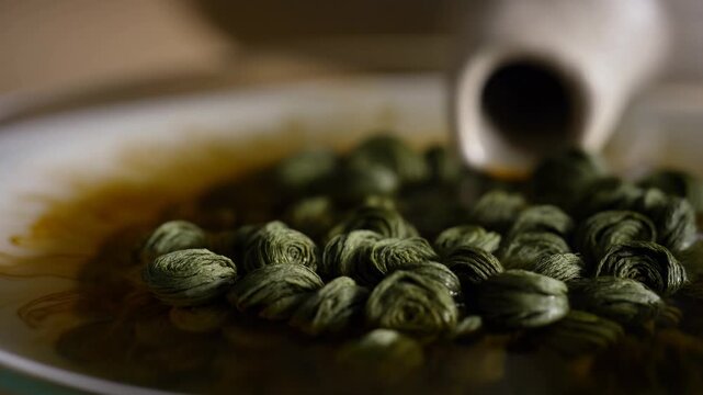 Pouring hot water over green tea leaves in cup: brewing process unfolds in three steps