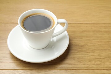 Aromatic coffee in cup on wooden table, closeup. Space for text