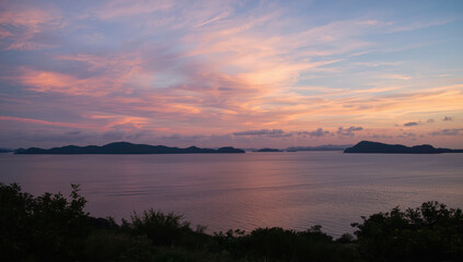 Fototapeta premium Serene pink sunset over calm coastal sea with distant island silhouettes and soft clouds