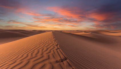 Vast desert dune ridge at sunset with colorful sky and textured sand
